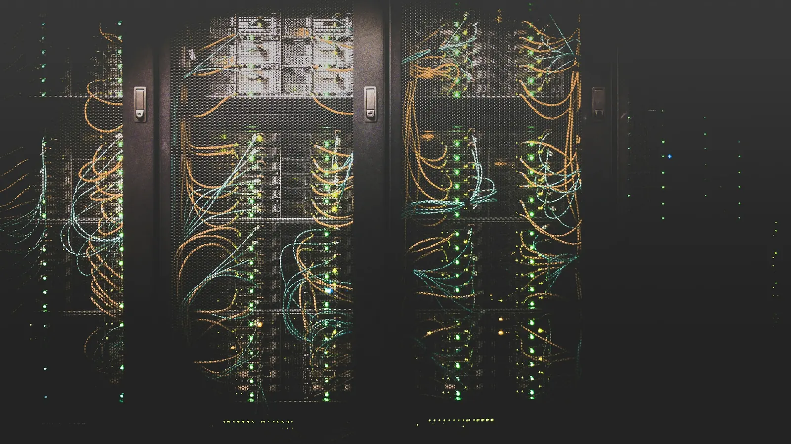 Data center server racks in low light, with network cables and status lights visible behind mesh doors