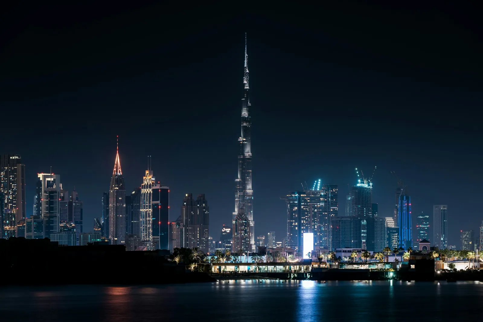 Downtown Dubai skyline at night, dominated by the world's tallest tower, with city lights reflected on the water